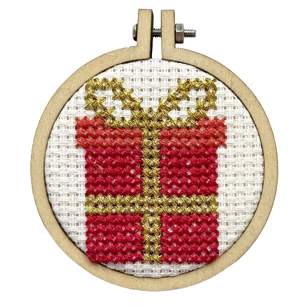 Cross-stitched red gift box with gold ribbon in a wooden hoop on a white background