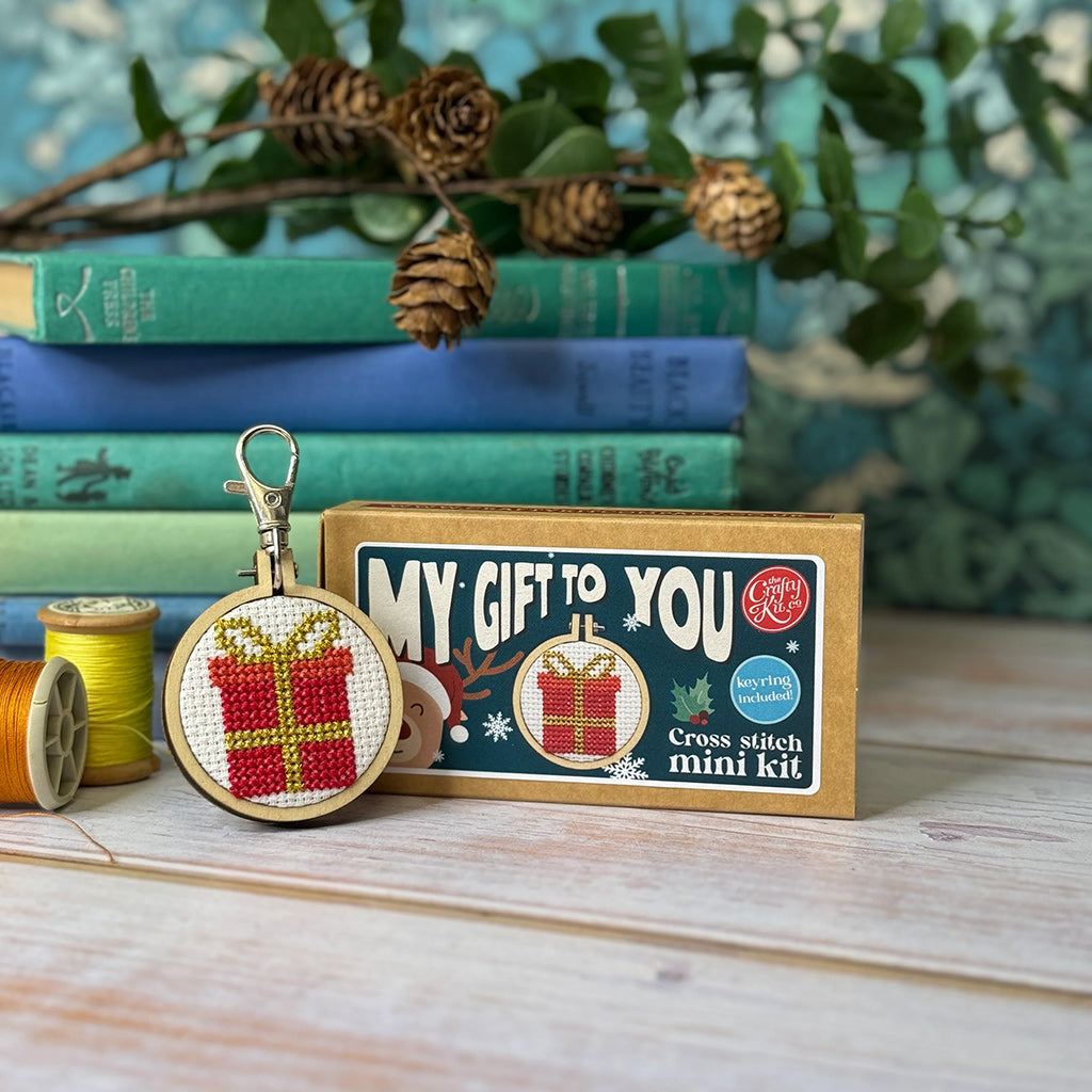 Cross stitch mini kit with a keychain and packaging labeled 'My Gift to You' on a wooden surface.