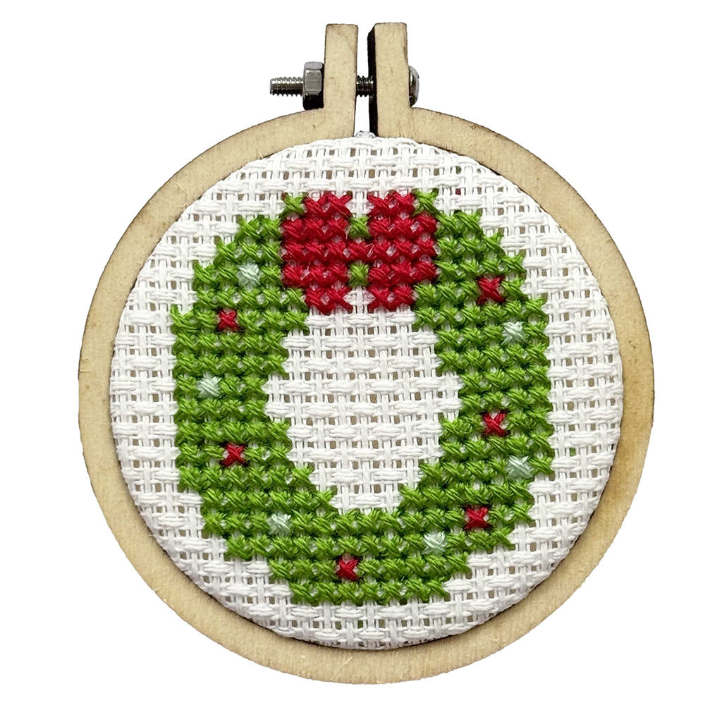 Embroidery hoop with a green wreath and red berries design on white fabric.