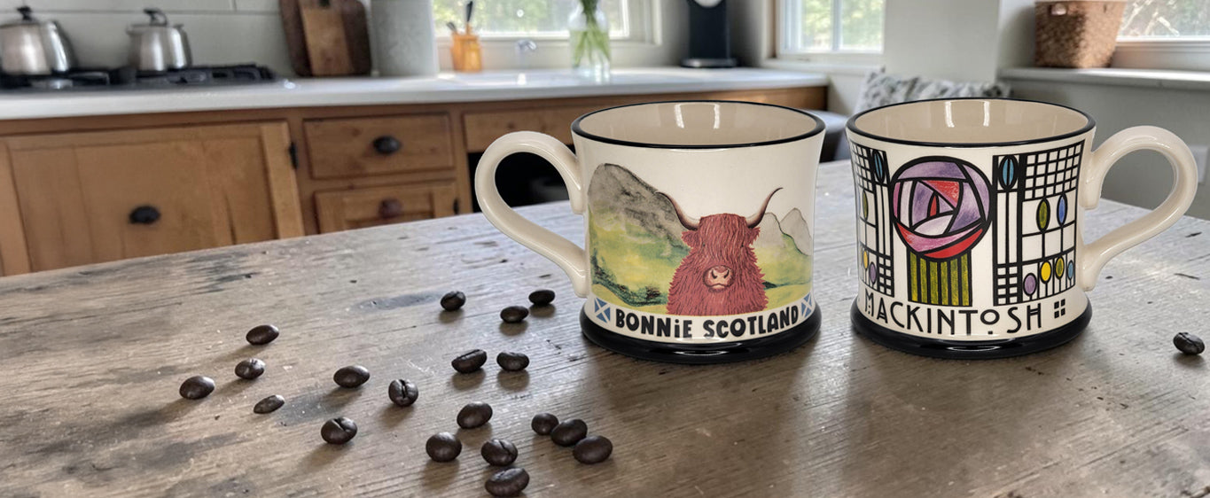 Two Moorland Pottery mugs with Scottish-themed designs on a kitchen counter with coffee beans.