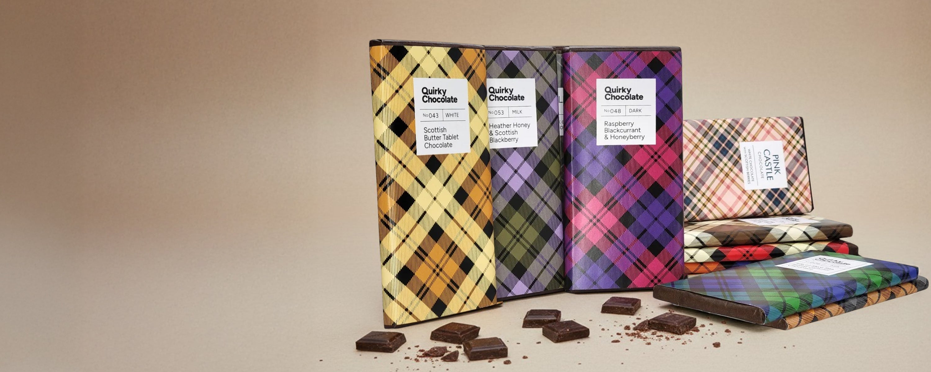 Quirky Chocolate bars with colourful plaid wrapping are displayed on a beige studio background, with several chocolate bars unwrapped and scattered in front.
