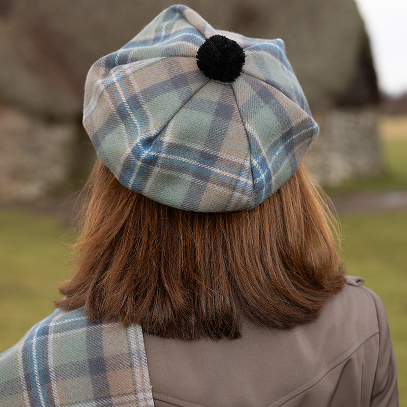 Person wearing a Spirit of Culloden Tartan cap with a black pom-pom in an outdoor setting