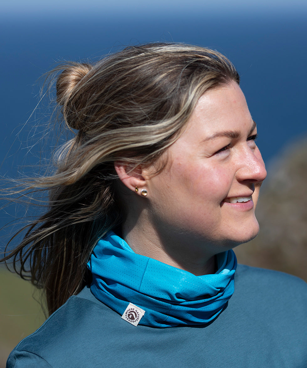 Woman wearing a 'Where Nature Leads' neck tube with a logo against a blue sky background