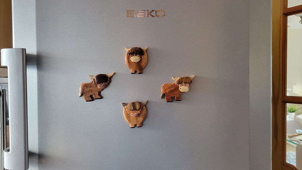 Fridge with wooden cow-shaped fridge magnets on a gray surface, featuring the collection