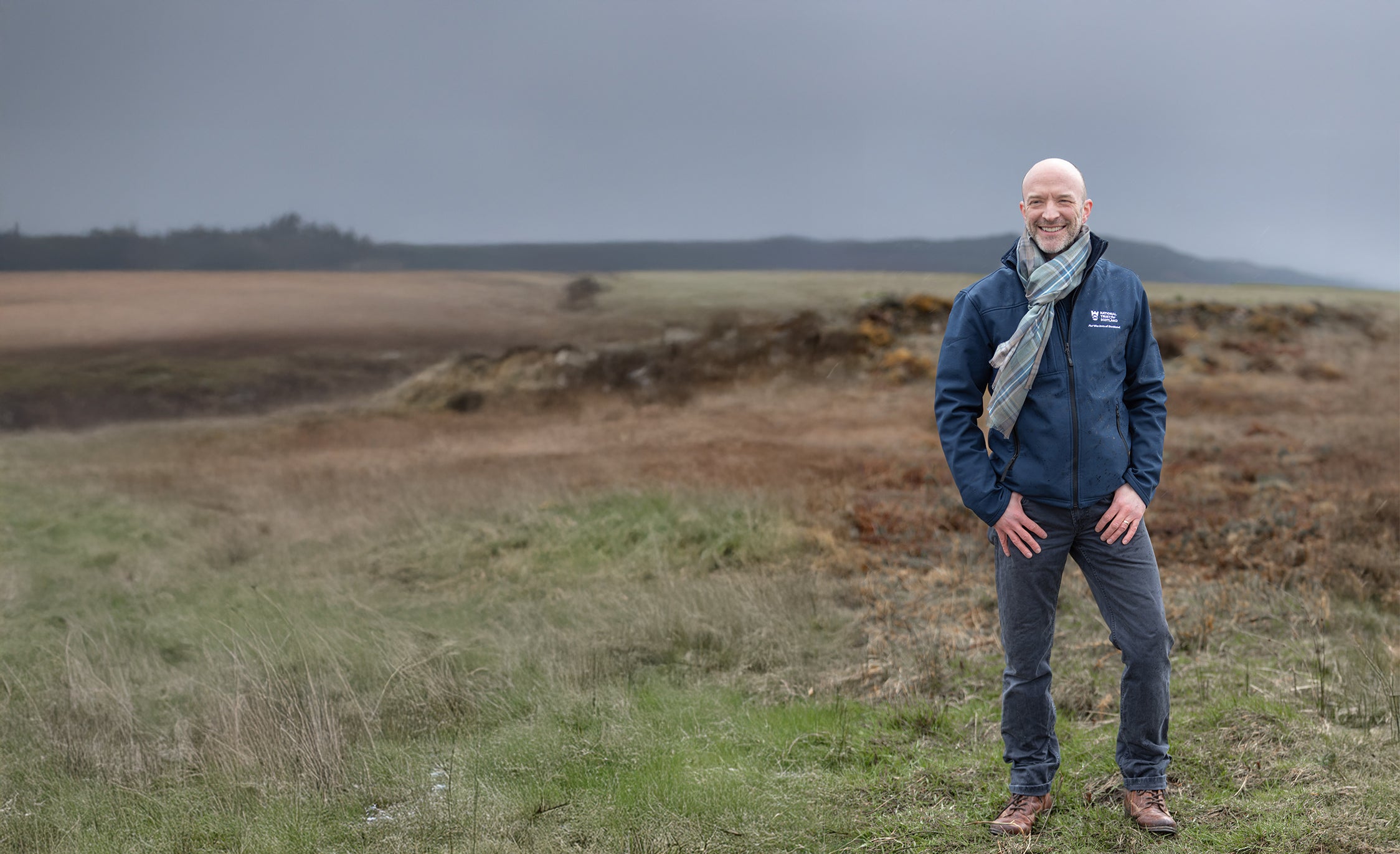 Man standing in a field wearing a Spirit of Culloden tartan scarf with a blurred background