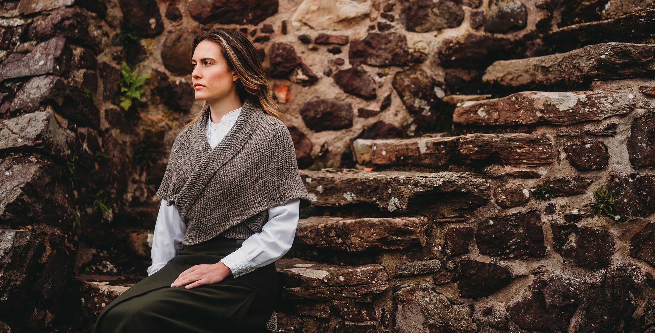 Woman in a Merino Wool Sontag Shawl, inspired by the Outlander series, sitting against a stone wall